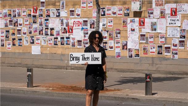 „Bringt sie nacht Hause“ steht auf dem Schild dieser Frau, die in Tel Aviv vor einer Wand mit den Fotos von Israelis steht, die von der Hamas im Gazastreifen gefangen gehalten werden.