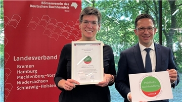 Das Foto zeigt eine Frau mit Urkunde und einen Mann mit DinA4-Blatt.