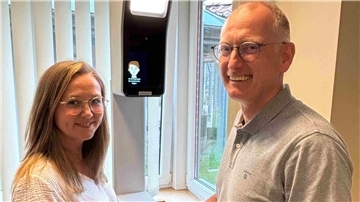 Eine Frau mit Brille und ein Mann mit Brille stehen vor einem Gerät. 
