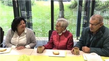 2 Frauen und ein Mann plaudern nebeneinander bei Kaffee und Topfkuchen.