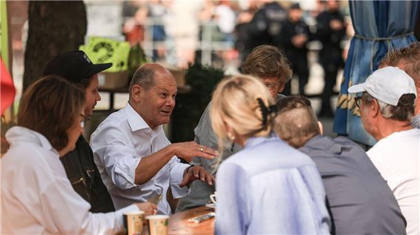 Bundeskanzler Olaf Scholz (M, SPD) spricht vor einem Büdchen mit Düsseldorfer Bürgern.