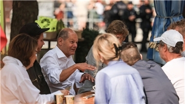 Bundeskanzler Olaf Scholz (M, SPD) spricht vor einem Büdchen mit Düsseldorfer Bürgern.