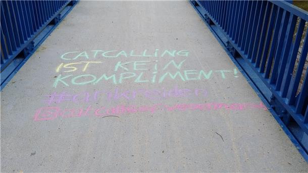 Eine Schrift mit Kreide auf einer Brücke mit blauem Geländer.