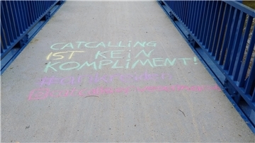 Eine Schrift mit Kreide auf einer Brücke mit blauem Geländer.
