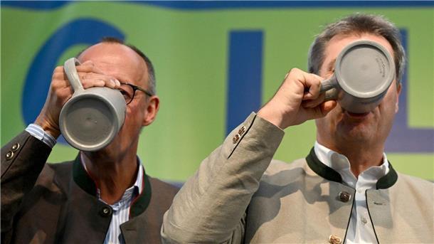 CDU-Chef Friedrich Merz (l) und Bayerns Ministerpräsident Markus Söder (CSU) trinken beim Politischen Frühschoppen Gillamoos auf der Bühne aus Bierkrügen.