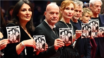Frauen und Männer in dunkler Kleidung stehen in einer Reihe und halten Fotos in den Händen. 