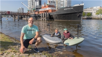Drei Personen posieren für ein Foto. Zwei davon sind mit Surfboards im Wasser.