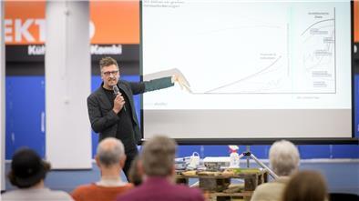 Christian Scheler steht vor einer Leinwand und erklärt.