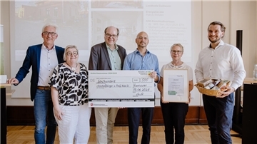 Gruppenfoto bei der Preisverleihung „Grüne Hausnummer 2024/2025“: Claudia Eßlinger und Ralf Habrik aus Nordleda halten einen großen Scheck über 500 Euro, eine Urkunde und einen Geschenkkorb in den Händen, flankiert von Gratulanten.
