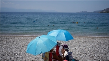 Da helfen nur noch Sonnenschrirme und ein Handventilator: Eine Frau am Strand von Loutraki.