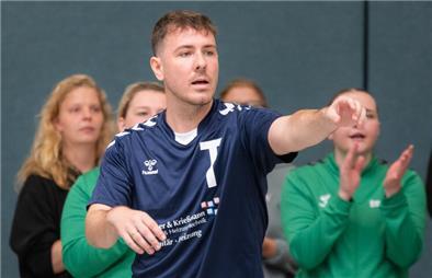 Ein Mann mit ausgestrecktem Arm im Trikot schaut an der Kamera vorbei und gibt Anweisungen. 