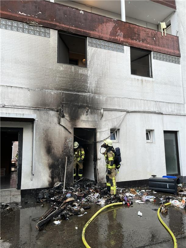 Zwei Feuerwehrleute stehen bei einem Haus, Ruß ist an der weißen Häuserwand zu sehen. Es handelt sich um einen Brand mehrerer Mülltonnen. Dank des schnellen Eingreifens der Feuerwehr konnte ein Übergreifen der Flammen auf das Wohngebäude in Lehe verhindert werden.