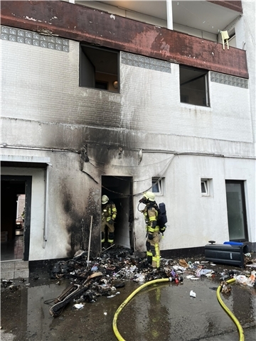 Zwei Feuerwehrleute stehen bei einem Haus, Ruß ist an der weißen Häuserwand zu sehen. Es handelt sich um einen Brand mehrerer Mülltonnen. Dank des schnellen Eingreifens der Feuerwehr konnte ein Übergreifen der Flammen auf das Wohngebäude in Lehe verhindert werden.