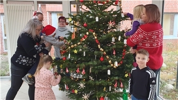 Erwachsene und Kinder hängen Schmuck an einen Weihnachtsbaum.