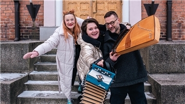 Drei Musiker stehen vor einem Backsteingebäude. 