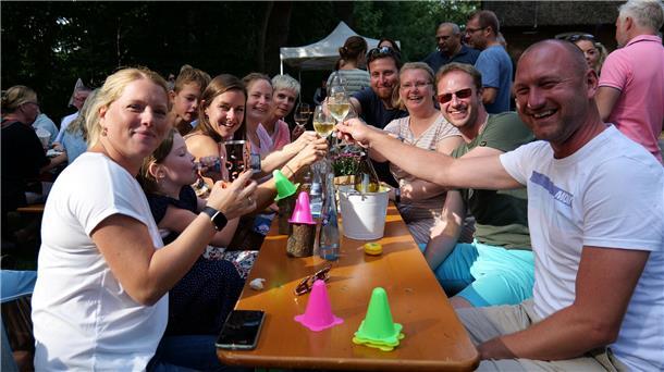 Menschen sitzen an einer Bierzelt-Garnitur und stoßen mit Weingläsern an.