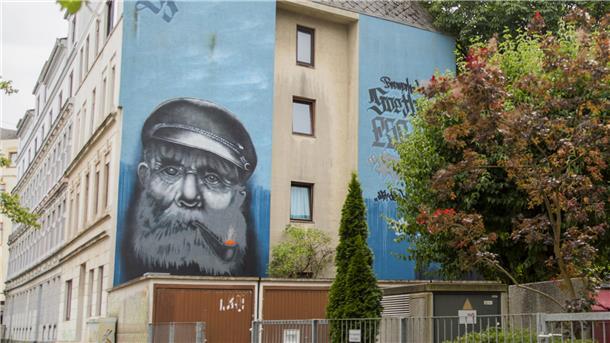 Eine Häuserfassade mit einem Graffiti, das einen alten Seemann mit Vollbart und Schiffermütze zeigt.