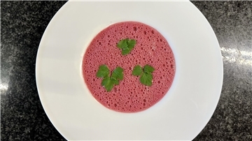 Ein weißer Teller mit pinker Rote Bete Suppe, garniert mit drei Blättern Petersilie. 