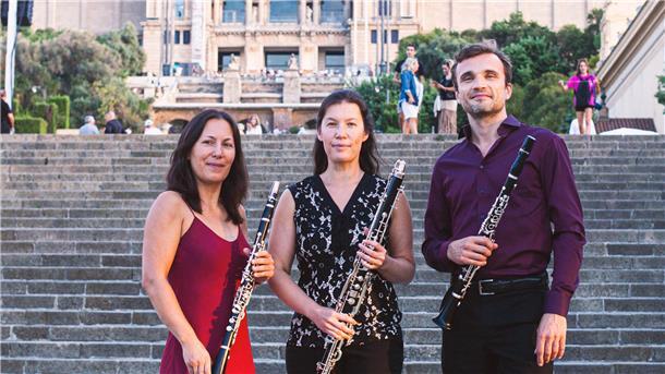 Zwei Frauen, ein Mann mit Klarinette in der Hand vor Steintreppe.