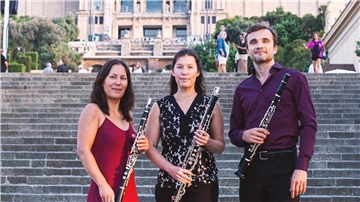 Zwei Frauen, ein Mann mit Klarinette in der Hand vor Steintreppe.