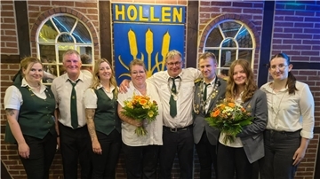 **ALT-Text:**
Gruppenfoto des neuen Königshauses des Schützenvereins Hollen: Acht Personen, teils in Uniform, stehen vor einem Schild mit der Aufschrift „Hollen“, zwei von ihnen halten Blumensträuße.