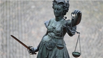 Eine Statue der Justitia hält eine Waage und ein Schwert in der Hand.