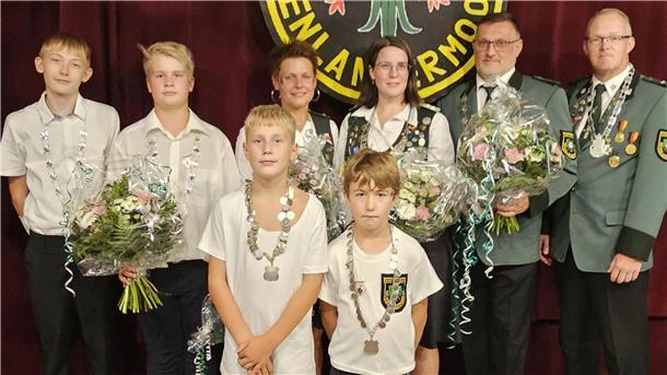**ALT-Text:**
Gruppenfoto der neuen Majestäten des Schützenvereins Neuenlandermoor: Acht Personen mit Schützenketten und Blumensträußen stehen vor einem Vereinswappen.