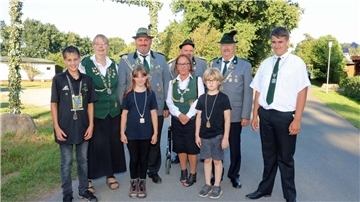Mehrere Erwachsene in Tracht und Uniform sowie drei Kinder stehen im Freien vor einem Baum.