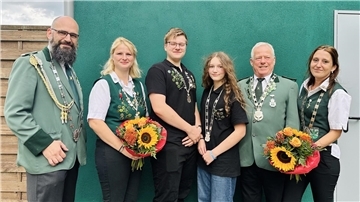 Gruppenfoto der neuen Schützenhoheiten des Schützenvereins Neuenlande. Drei Männer und drei Frauen tragen Schützenketten, zwei Frauen halten bunte Blumensträuße mit Sonnenblumen. Alle stehen vor einer grünen Wand und lächeln in die Kamera.