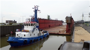 Ein blauer Schlepper und ein rotes Schwimmdock liegen in einer Schleuse
