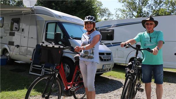 Zwei Urlauber stehen mit ihren Fahrrädern vor Wohnmobilen.