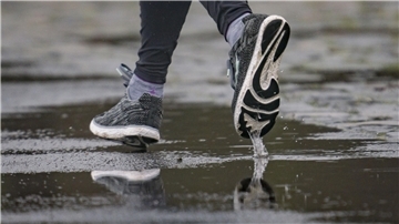Die Füße eines Joggers spiegeln sich in einer Pfütze.