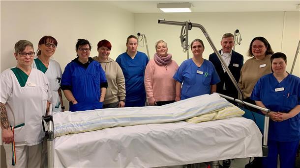 Zehn Menschen stehen hinter einem Krankenhausbett.