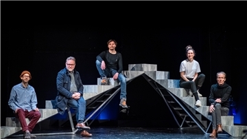 Die fünf Schauspieler sitzen auf einer Treppe und schauen in die Kamera.