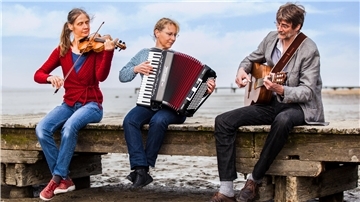 Drei Musiker sitzen mit ihren Musikinstrumenten auf eiem Steg. 