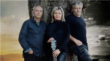 zwei Männer und eine Frau mit Gitarre lehnen an einem Baum