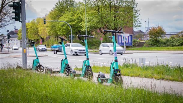 So buchen Sie eine Fahrt mit dem E-Roller in Bremerhaven (Video) Vier E-Roller stehen in einer Reihe an einer vielbefahrenden Straße in Bremerhaven.