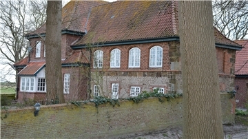 Altes Pfarrhaus, davor eine Mauer und Bäume.