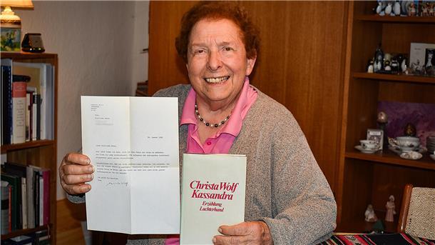 Eine ältere Frau hält ein Buch und einen Brief in der Hand.