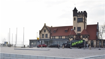 Ein Gebäude mit einem Turm steht an der Weser. Darum ein Bauzaun. Vor dem Gebäude stehen drei Autos.