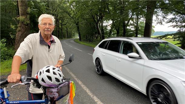 Ein Mann steht mit seinem Fahrrad neben einer Landstraße.