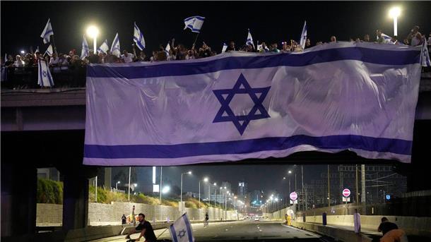 Justizreform in Israel schreitet voran - Herzog in den USA Demonstranten haben bei ihren Protesten eine riesige Nationalfahne an einer Autobahnüberführung in Tel Aviv aufgehängt.