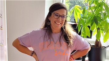 Eine lachende Frau mit Brille und dunklen langen Haaren.