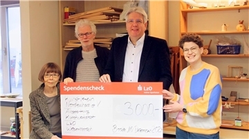 Zwei Frauen und zwei Männer halten in einer Werkstatt einen symbolischen Scheck in den Händen.