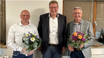 Drei Männer, zwei von ihnen halten je einen Blumenstrauß in den Händen.