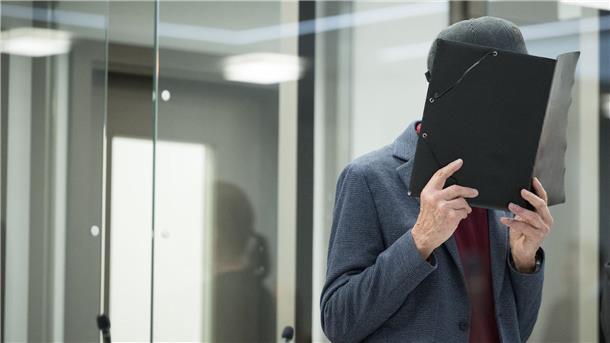 Mord aus dem Hinterhalt: Ex-Stasi-Mitarbeiter bestreitet Tat Der Angeklagte hält sich zu Beginn des Prozesses eine Mappe vors Gesicht. Der 80-Jährige will sich zu den Vorwürfen nicht äußern.