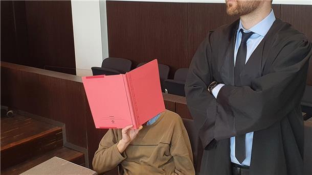 „Cold Case“ - Prozess um „Mord im Maisfeld“ gestartet Der Angeklagte (l) sitzt neben seinem Verteidiger Maximilian Klefenz im Verhandlungssaal des Düsseldorfer Landgerichts und verdeckt sein Gesicht.