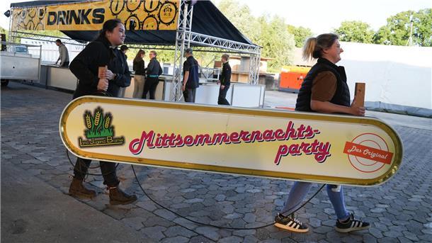 Zwei Frauen tragen in Bramel ein Schild mit der Aufschrift Mittsommernachtsparty.