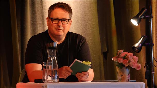 Das ist am Wochenende in Bremerhaven und im Landkreis Cuxhaven los Ein Mann sitzt auf einer Bühne und hält ein Buch in den Hönden. Er blickt in die Kamera. Der Bremerhavener Autor Olaf Satzer liest in Beverstedt aus seinem Roman „Wehrbach“. Musikerin Dahlia Crimson begleitet die Veranstaltung mit dunklen Klangwelten zwischen Rock und Dark Wave.