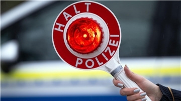Eine Polizistin hält während einer Verkehrskontrolle eine Polizeikelle mit der Aufschrift „Halt Polizei“.